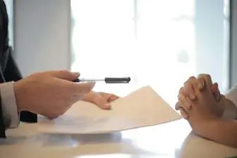 Consulting services thumbnail: a consultant offering a pen and paper to a client on the other side of a table.